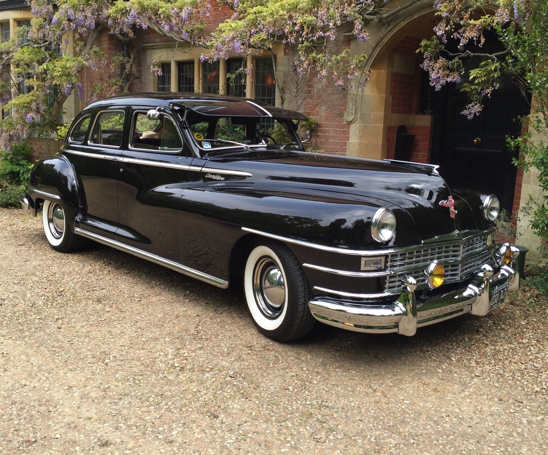 Black vintage Chrysler car parked in front of a stone building with flowering vines.