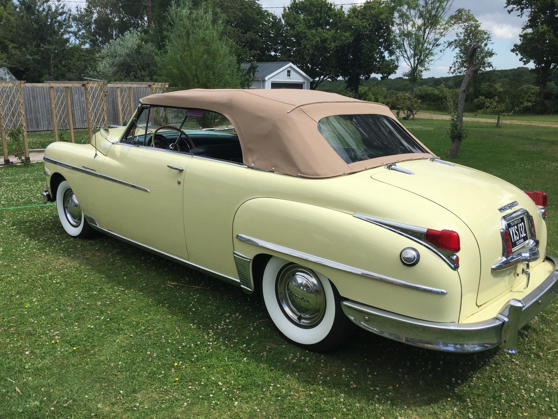 Yellow vintage convertible car with a tan roof parked on grass.
