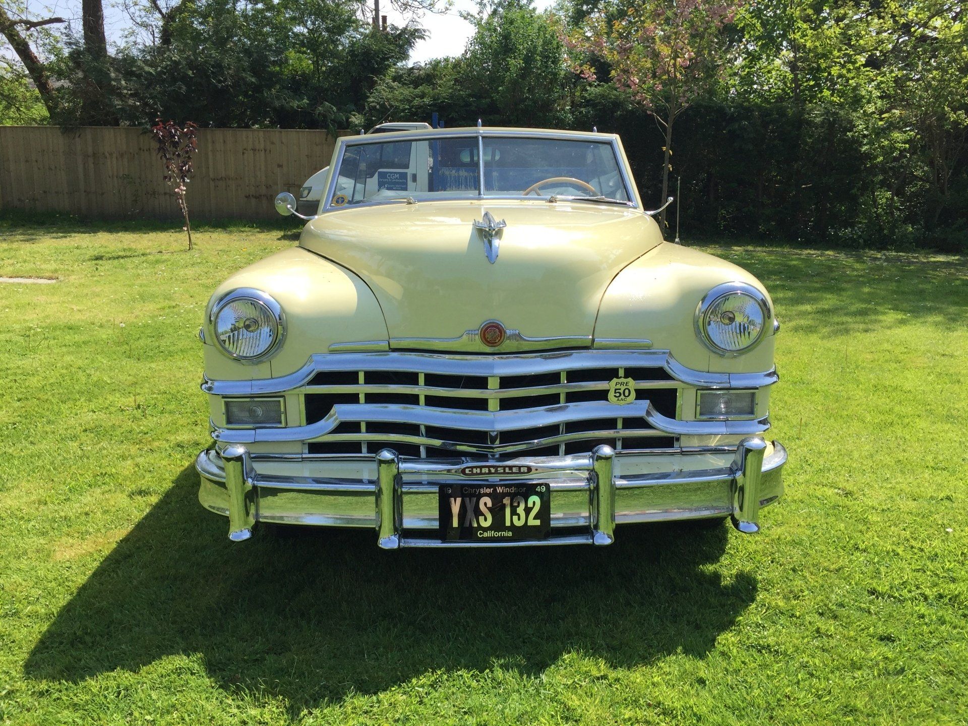 Yellow convertible classic car parked on a grassy lawn; sunny day.