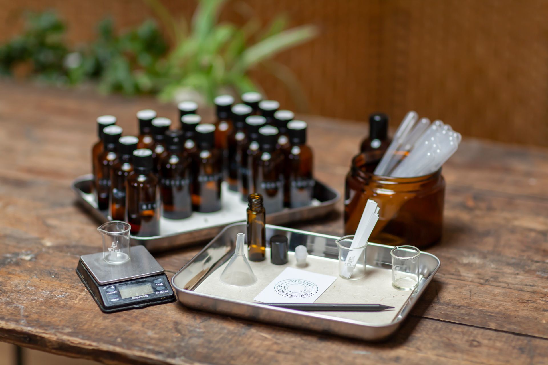 Bottles and equipment for scent making on a wooden table, including a scale, funnels, and droppers.