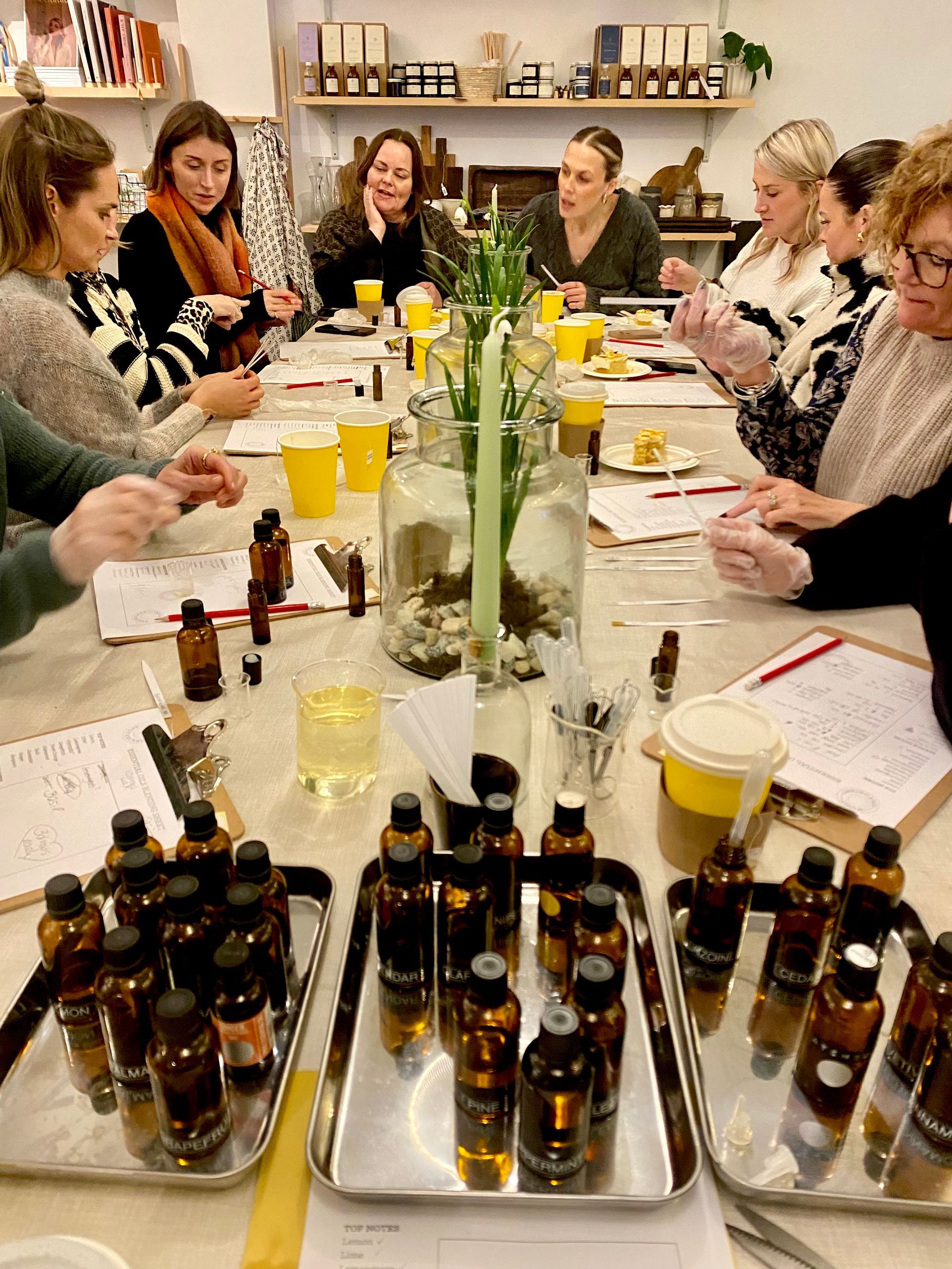 People gathered around a table with essential oil bottles, notebooks, and glassware, participating in a workshop.