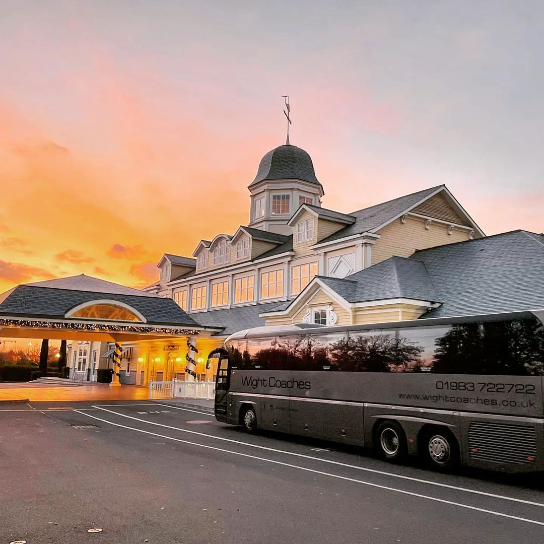Bus parked in front of a grand hotel at sunset, with a colorful sky.