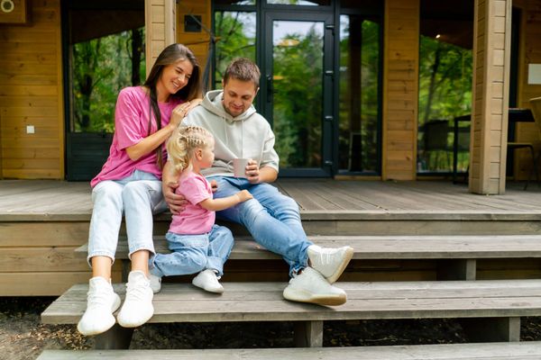 A family is sitting on the porch of a house looking at a tablet.