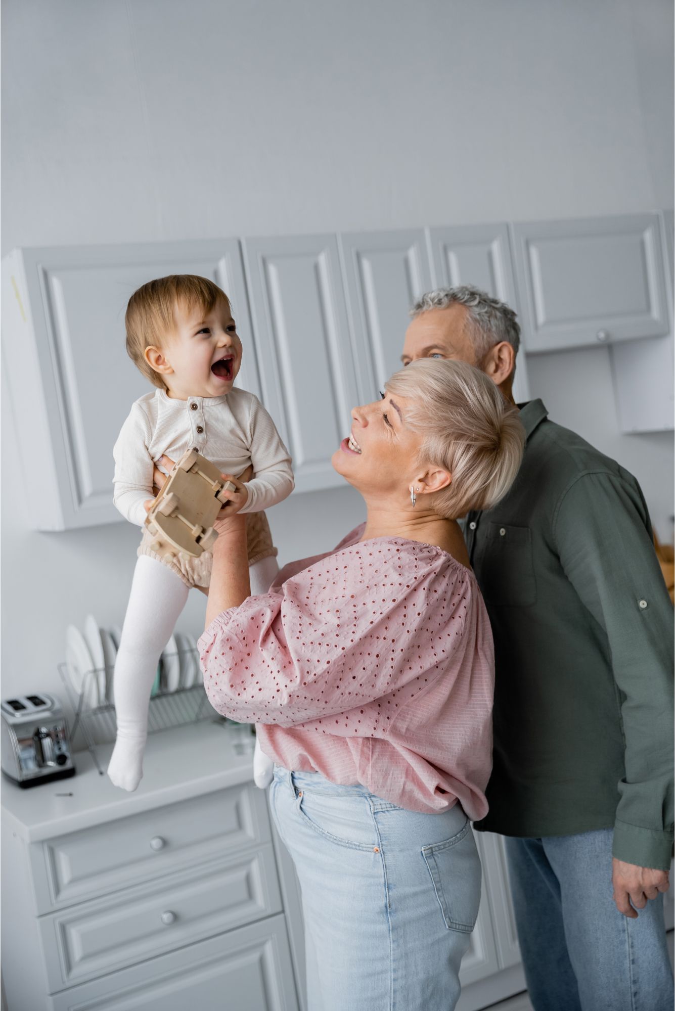 An elderly couple is holding a baby in their arms in a kitchen.