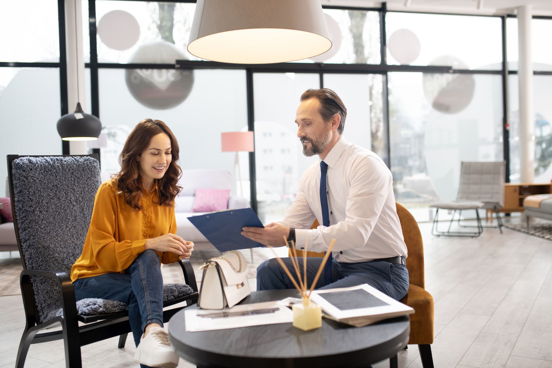 A man and a woman are sitting at a table looking at a clipboard.