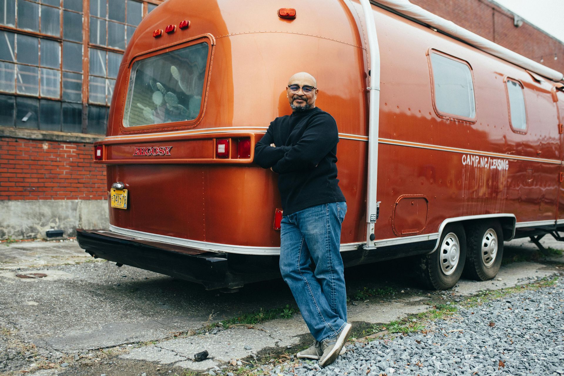 A man is leaning against a red airstream trailer.