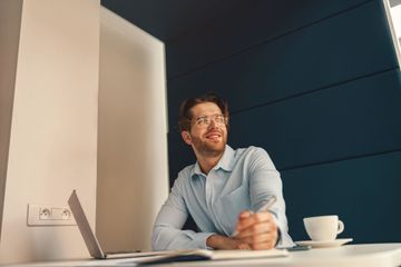 A man is sitting at a desk with a laptop and a cup of coffee.