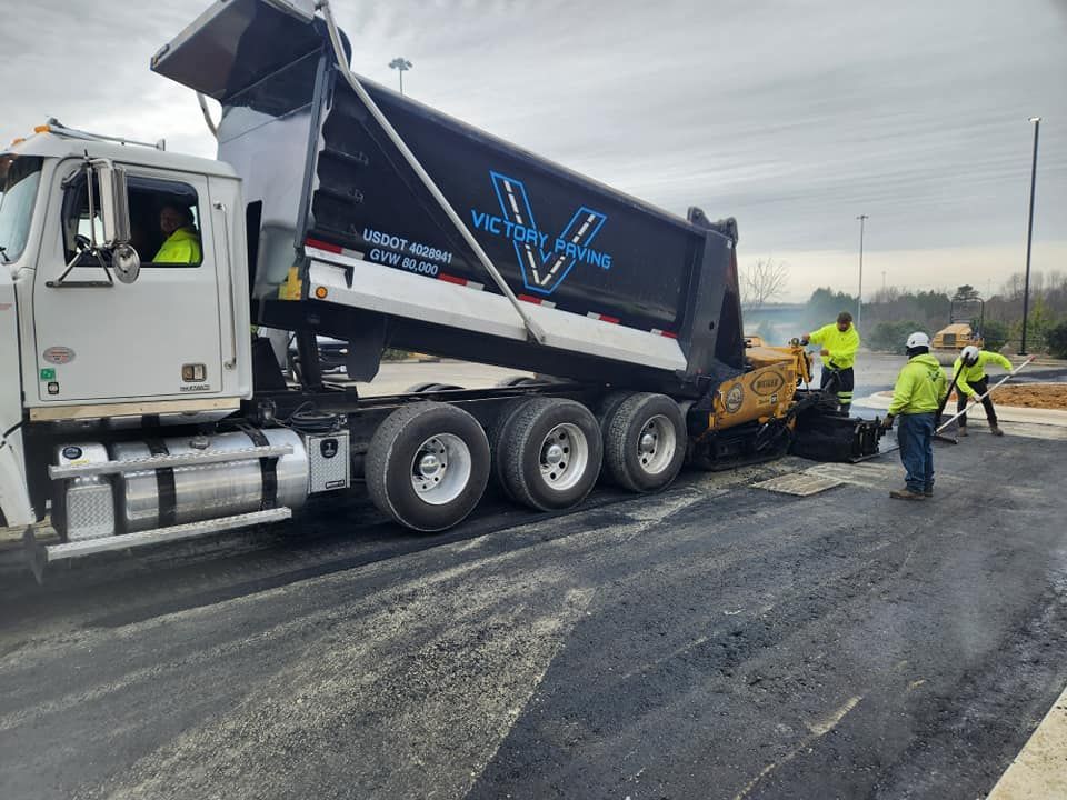 A dump truck is being loaded with asphalt on a road