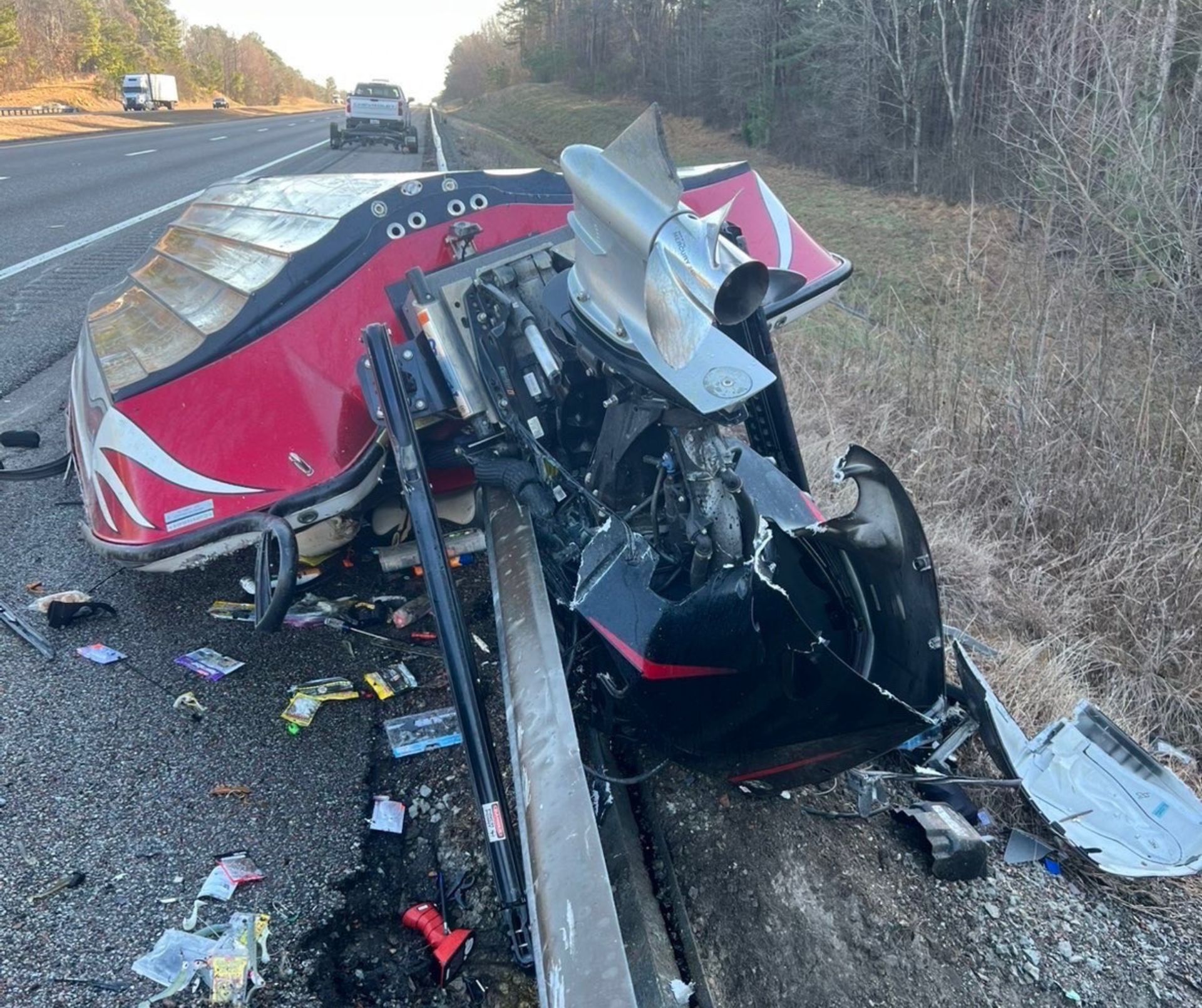 Severely wrecked red semi-truck on highway shoulder with debris scattered around and mangled front end