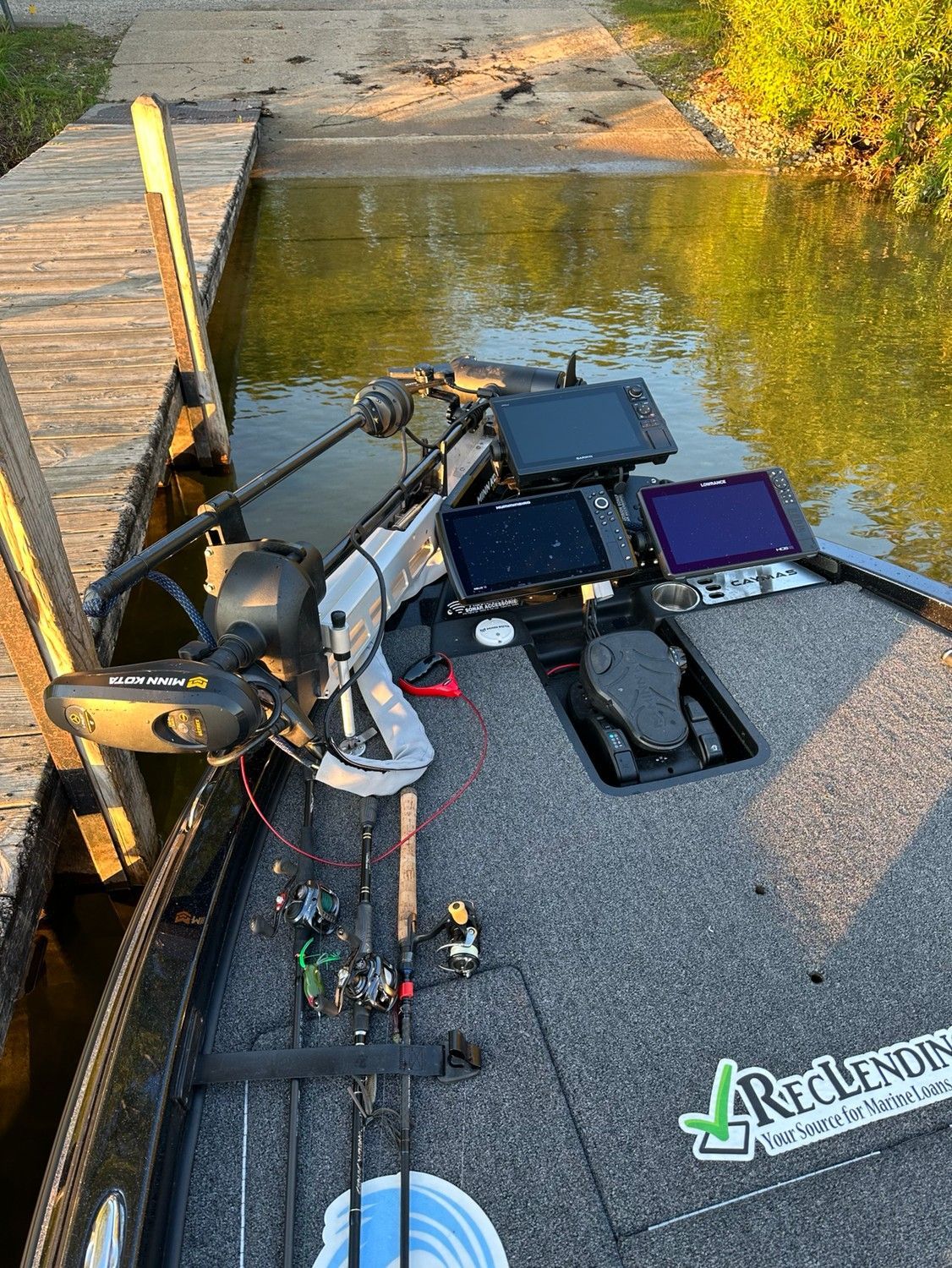 Fishing gear and a chair on a dock beside calm water at sunrise