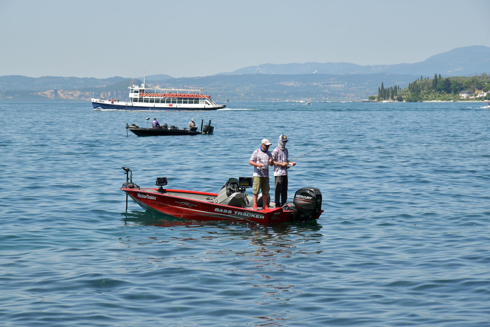 Small red motorboat with people on blue water, with a larger boat and coastline in the background