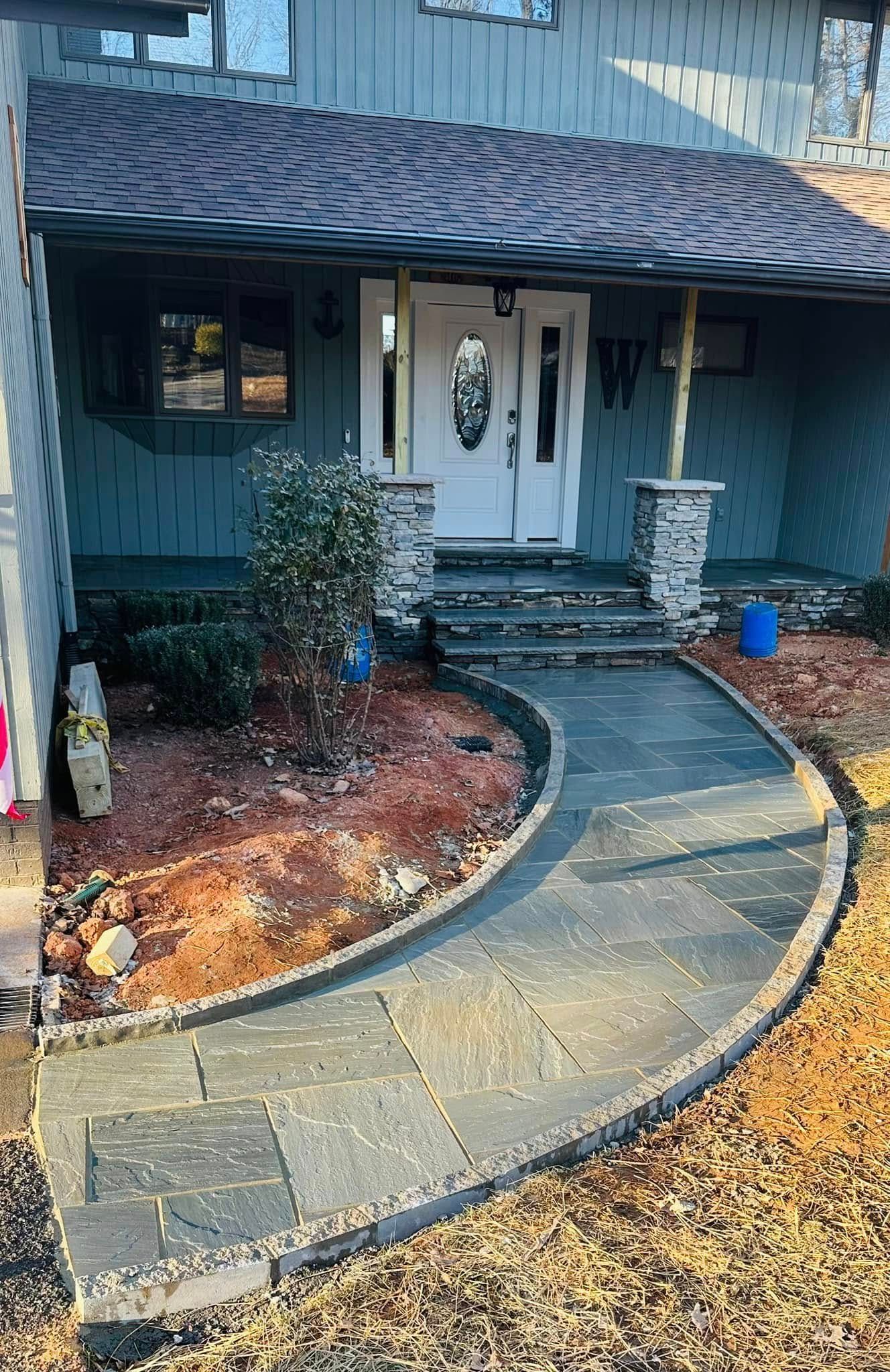 Curved stone walkway leading to a blue house with a white front door and small front garden