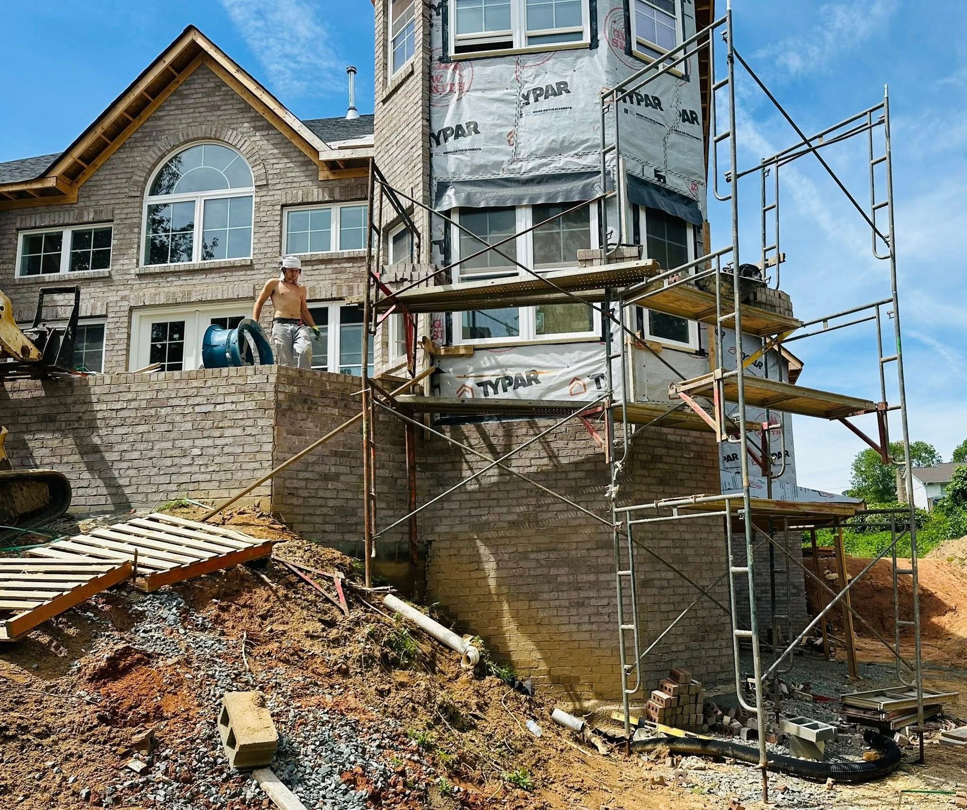 Stone house under construction with scaffolding, exposed brick, and a pile of rubble in front.