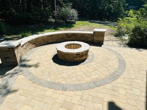 Circular stone fire pit and curved bench on a paved patio surrounded by greenery