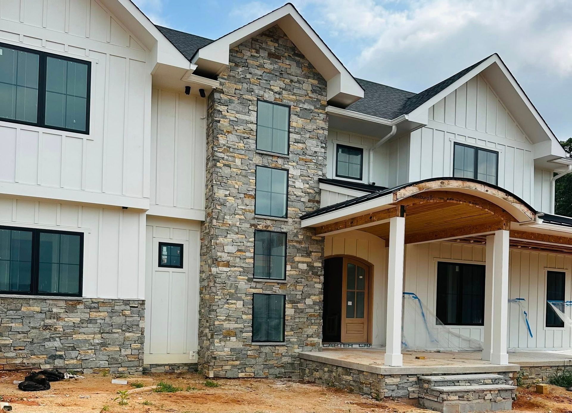 Modern two-story stone and white house exterior with a covered front porch and large windows