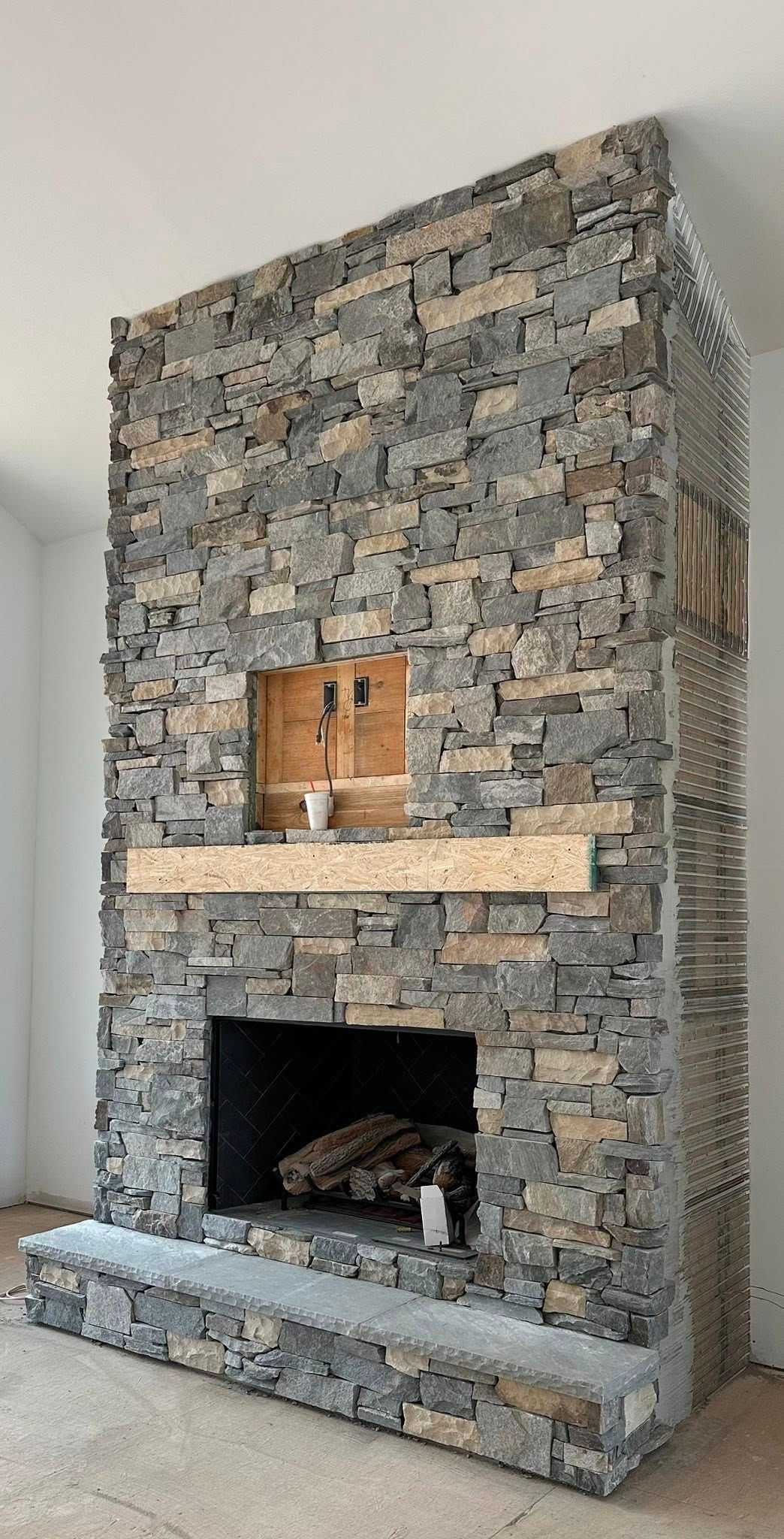 Stone-faced fireplace with a metal insert and wooden log storage in a modern room