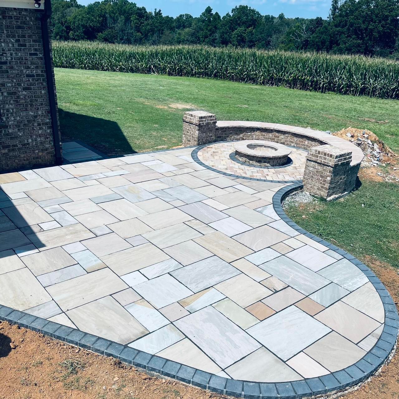 Curved stone patio with a circular fire pit and built-in bench in a grassy backyard.