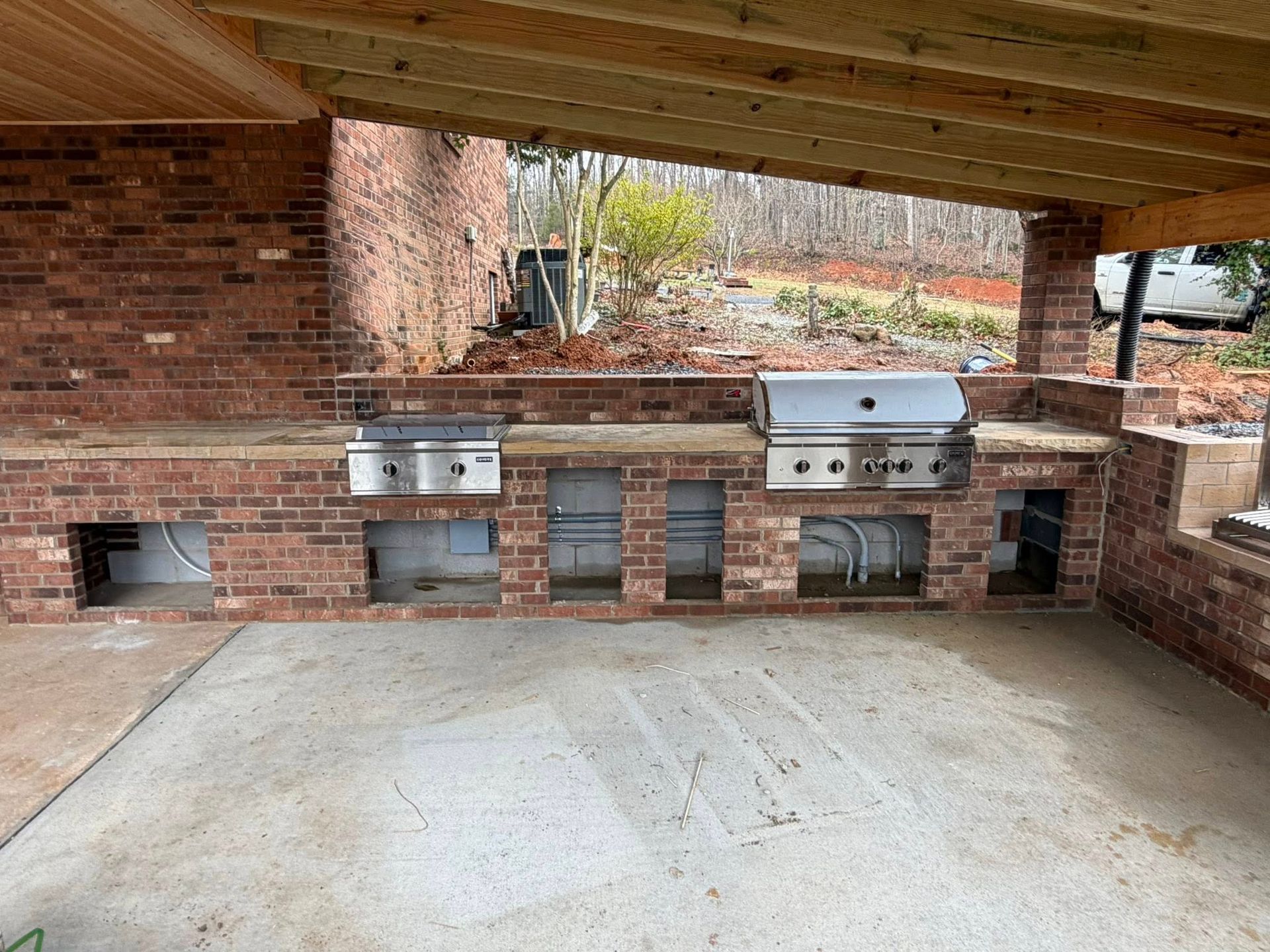 Covered brick outdoor patio with built-in stainless steel grills and sinks along the back wall