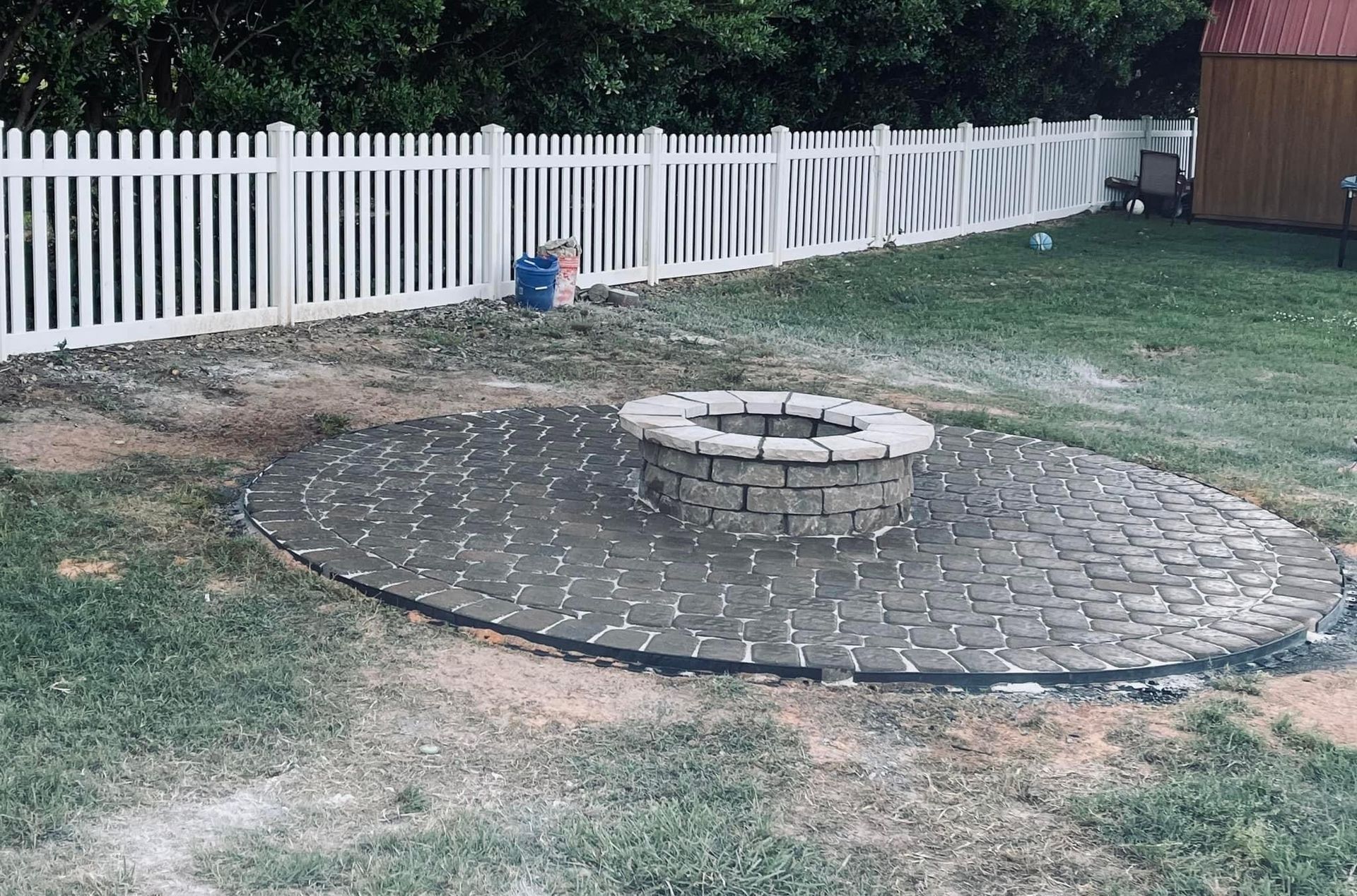 Backyard patio with circular stone fire pit and a white picket fence