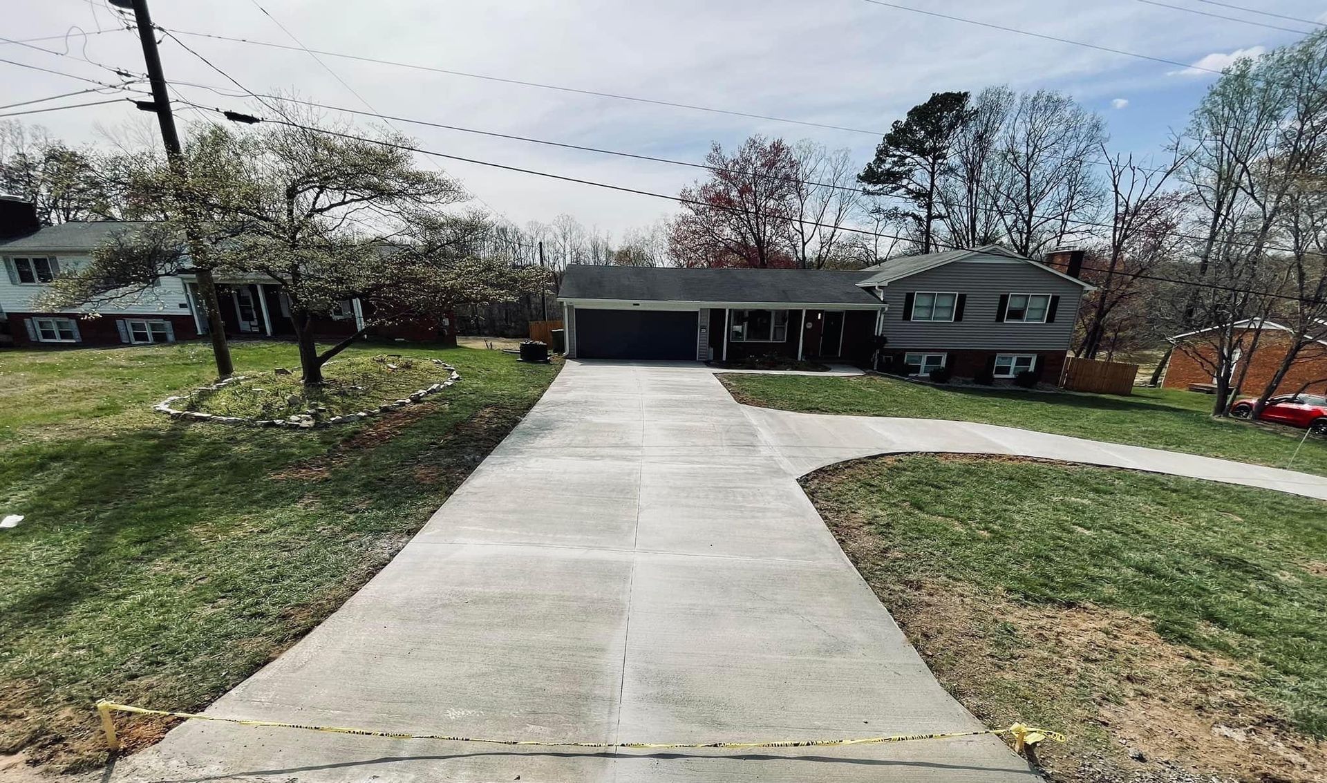 Concrete driveway leading to a carport beside a house, with lawns and trees on both sides.