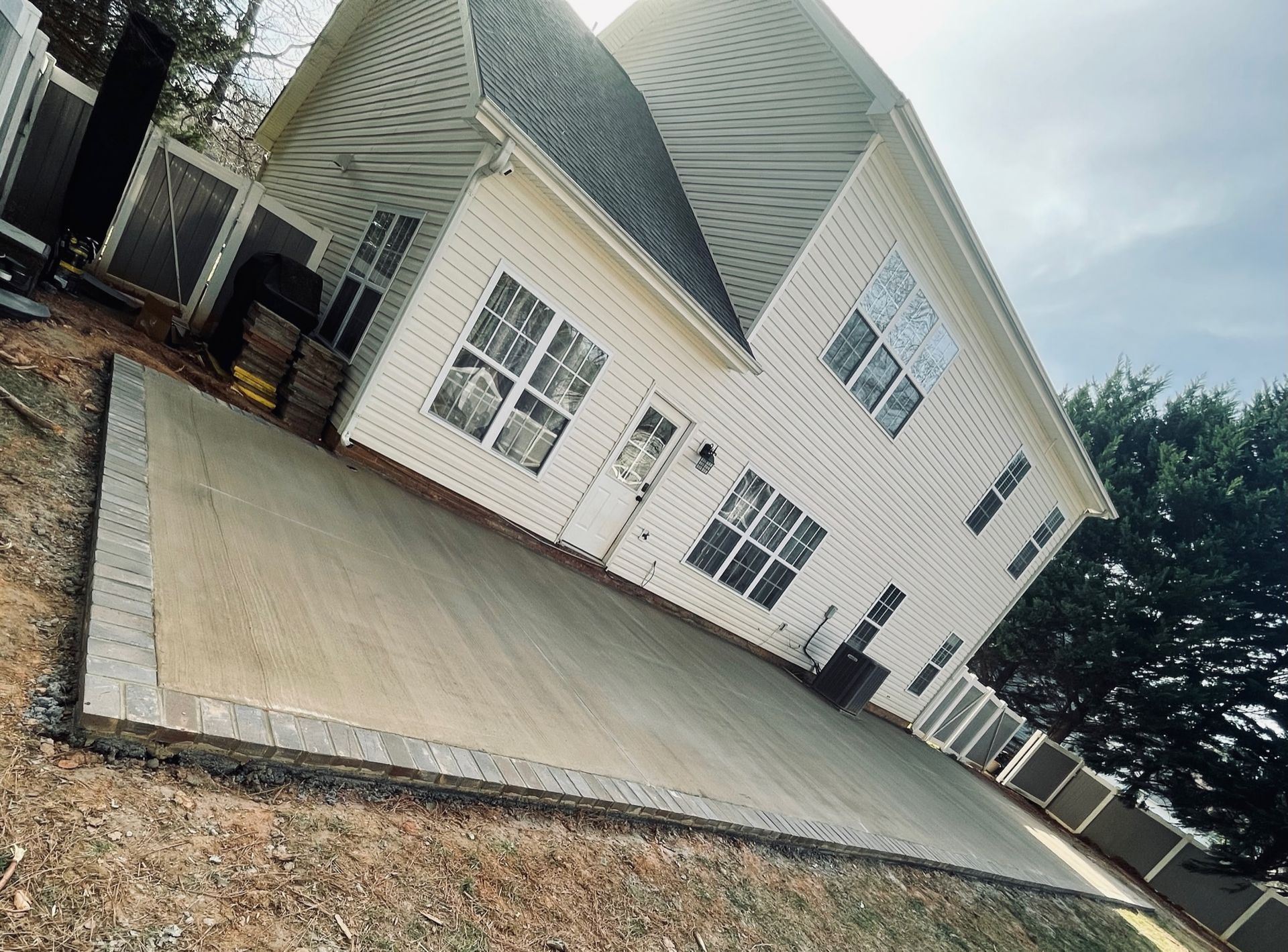 Tilted view of a white house with a large concrete patio and gravel yard under a cloudy sky