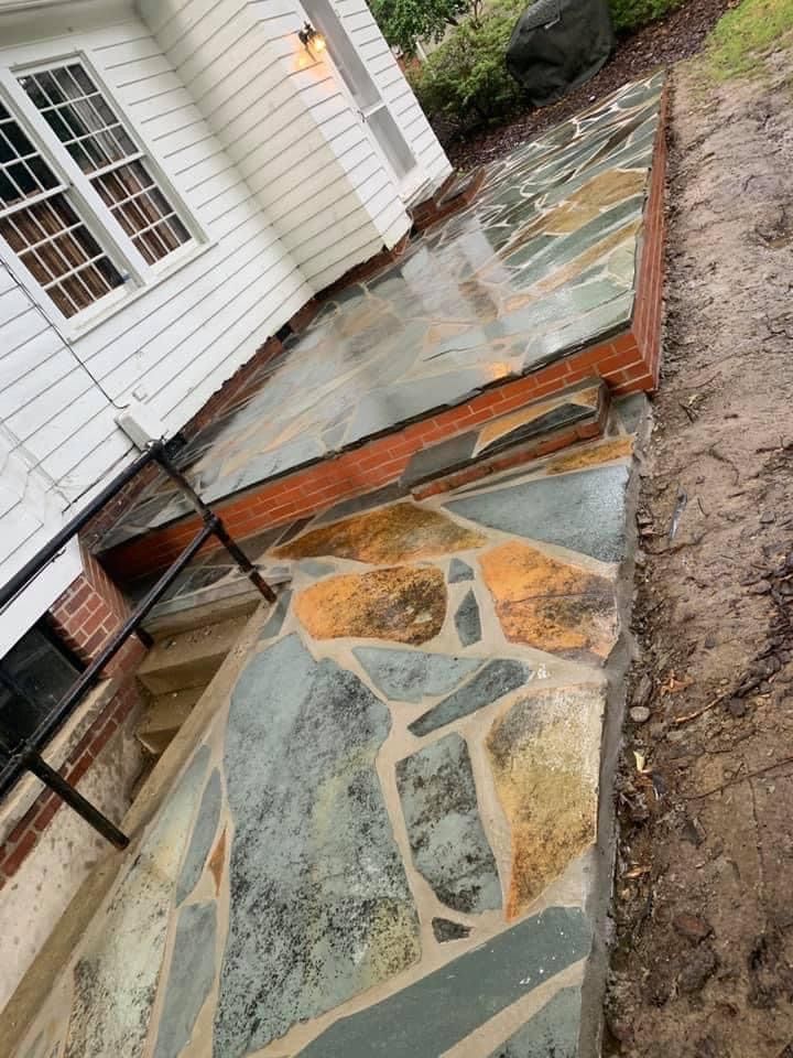 Stone walkway beside a white house, with brick edging and exposed dirt on one side.