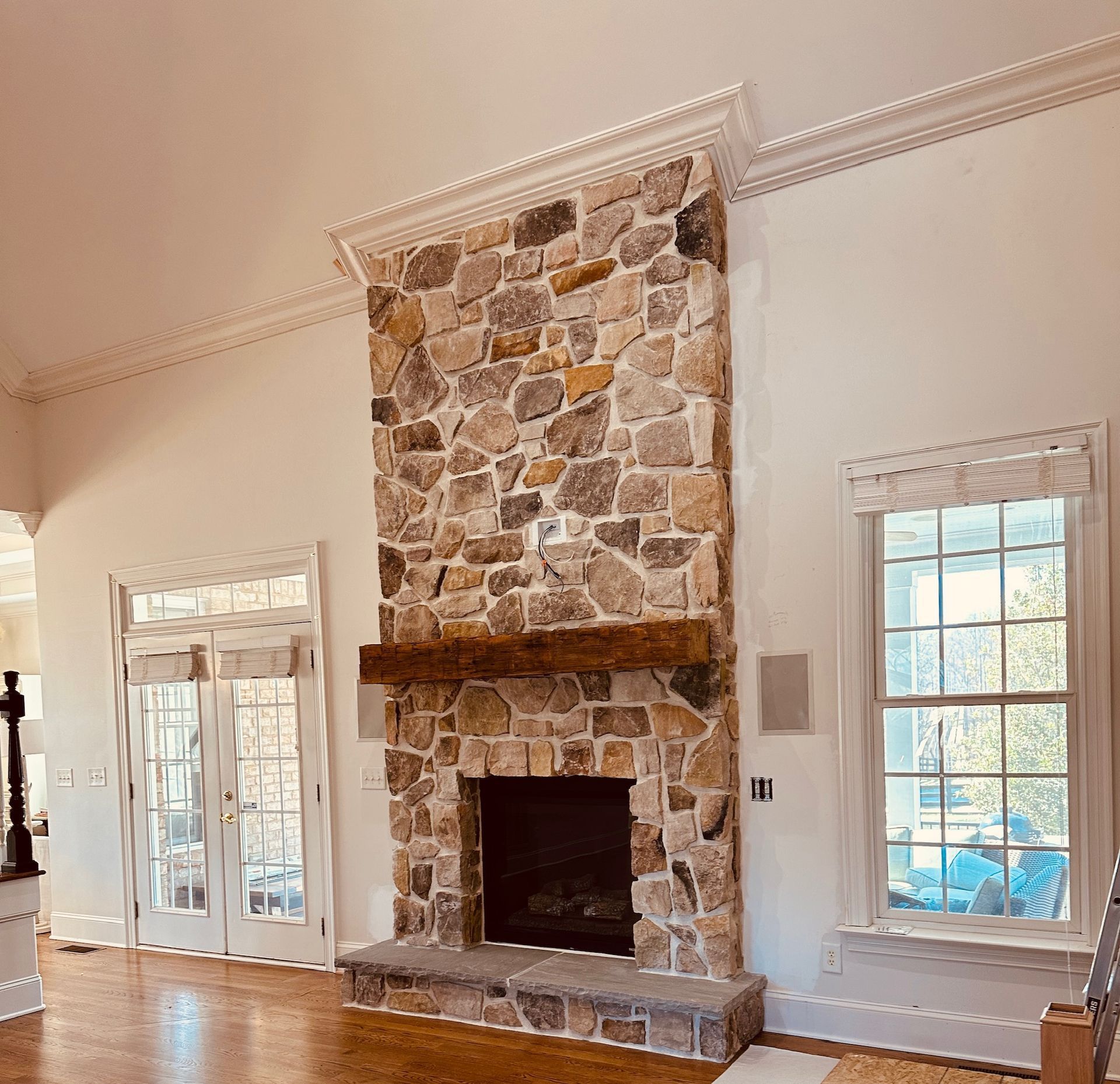 Bright living room with a stone fireplace and large windows, hardwood floors, and white trim.
