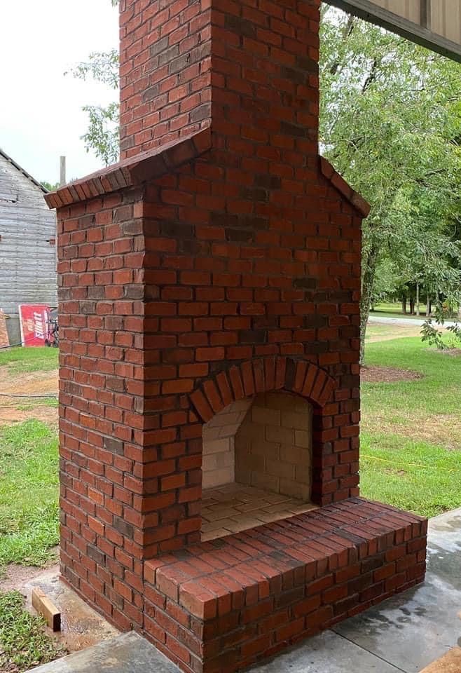 Brick outdoor fireplace with arched opening and chimney under a covered patio, surrounded by grass.