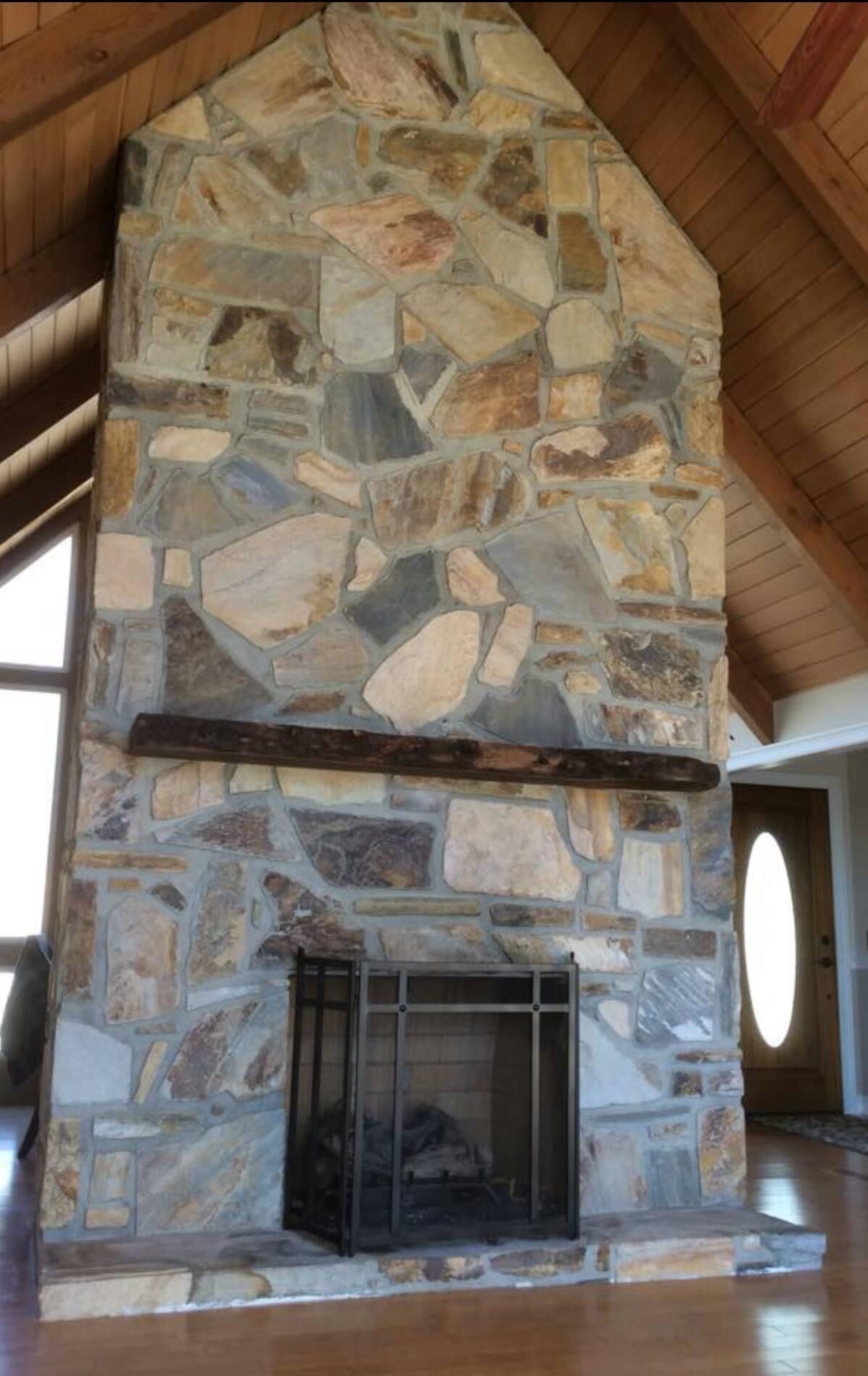 Rustic stone fireplace with a black metal firebox under a wooden vaulted ceiling