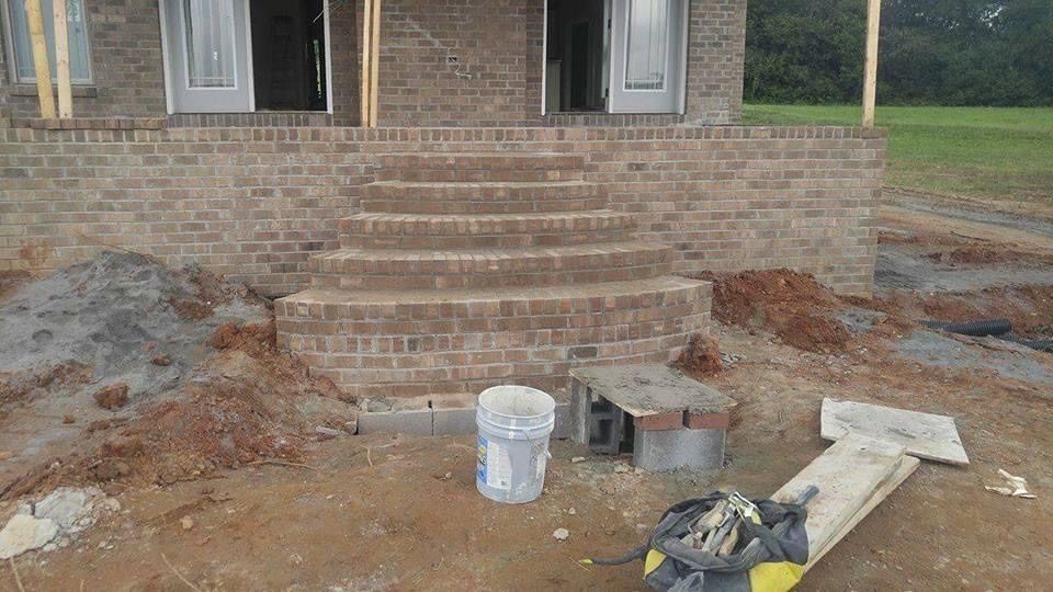 Brick house front steps under construction with tools, bucket, and dirt in the yard