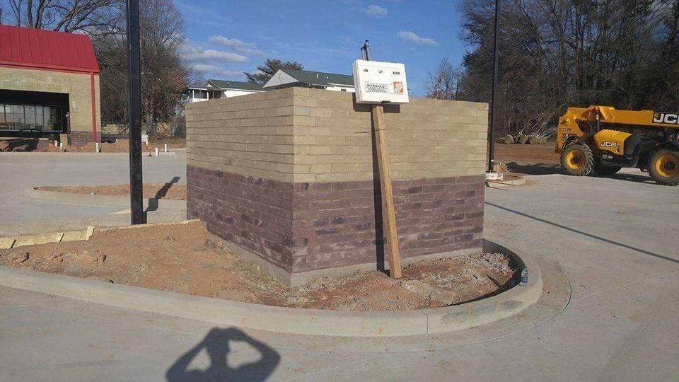 Brick monument sign at a roadside curb, with a yellow construction vehicle in the background.