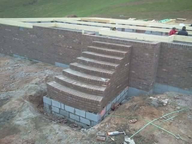 Brick steps built into a retaining wall at a construction site, with dirt and unfinished ground nearby