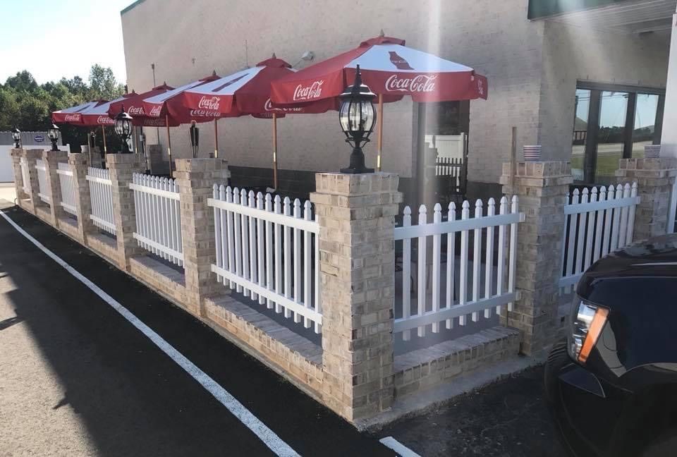 Outdoor patio with red Coca-Cola umbrellas behind a white picket fence beside a building