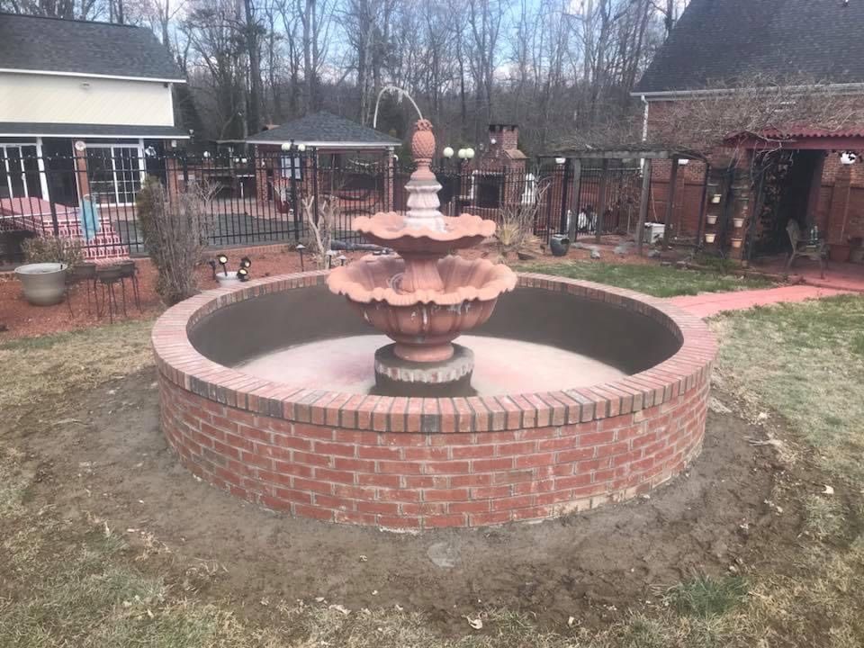 Brick fountain in a circular garden bed in a backyard with patio and pergola.