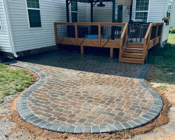 Curved brick patio with gray border stones beside a wooden deck and house siding
