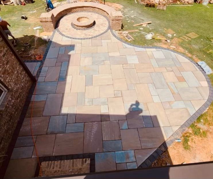 Patio with stone pavers and a circular fire pit, seen from above, with a shadow in the foreground