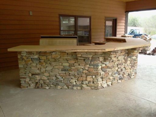 Stone-faced outdoor bar with a wooden countertop on a covered patio