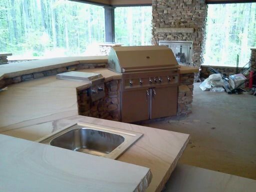 Unfinished kitchen with granite counters, sink, and large grill by windows in a wooded setting