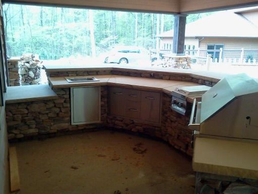 Covered outdoor kitchen with stone counters and built-in grill overlooking a yard