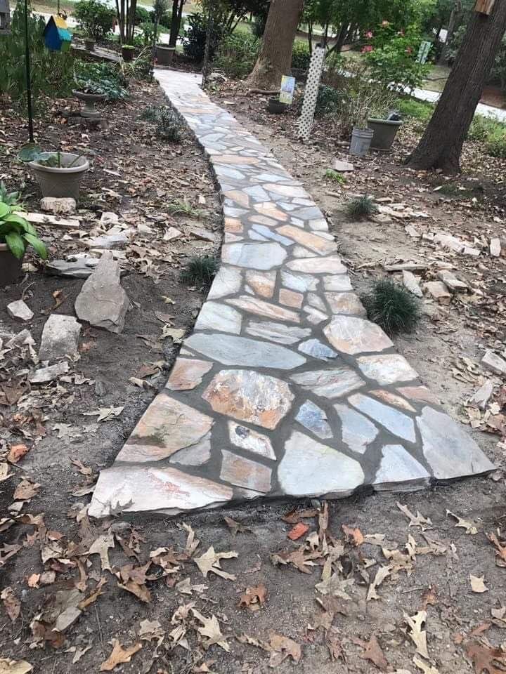 Stone walkway curving through a wooded garden with leaves scattered on the ground
