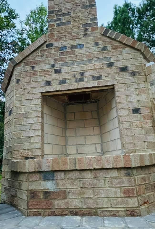 Stone outdoor fireplace with a brick chimney and open firebox against a blue sky