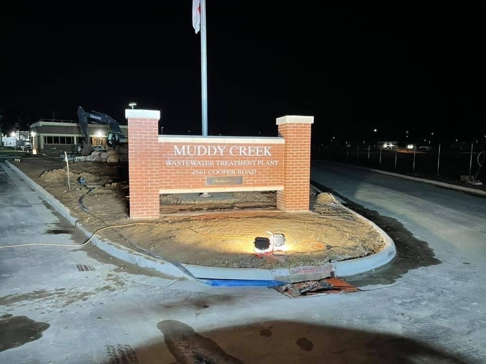 Muddy Creek entrance sign at night with brick columns and a lit landscaped island