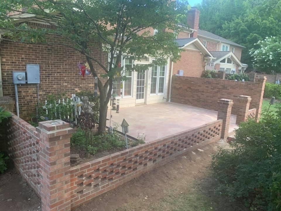 Brick patio with low decorative wall, trees, and a house entrance with glass doors