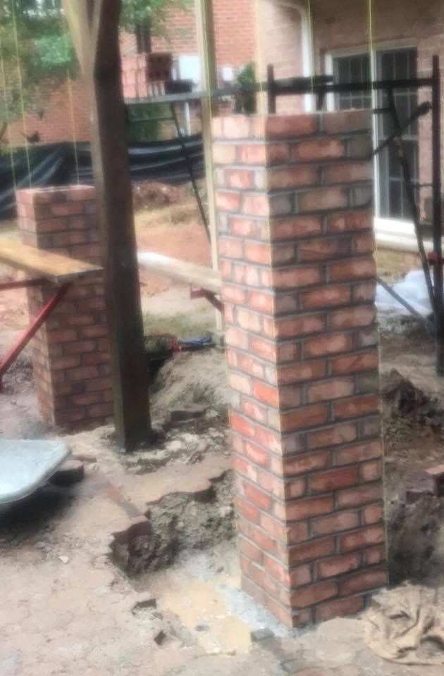 Brick porch column under construction in a muddy yard with scaffolding and debris