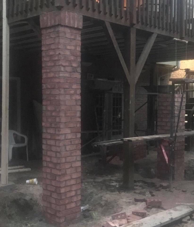 Brick house patio with wooden balcony, table, and chairs under the deck