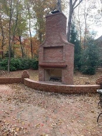 Brick outdoor fireplace in a wooded park with a curved brick bench and fallen autumn leaves
