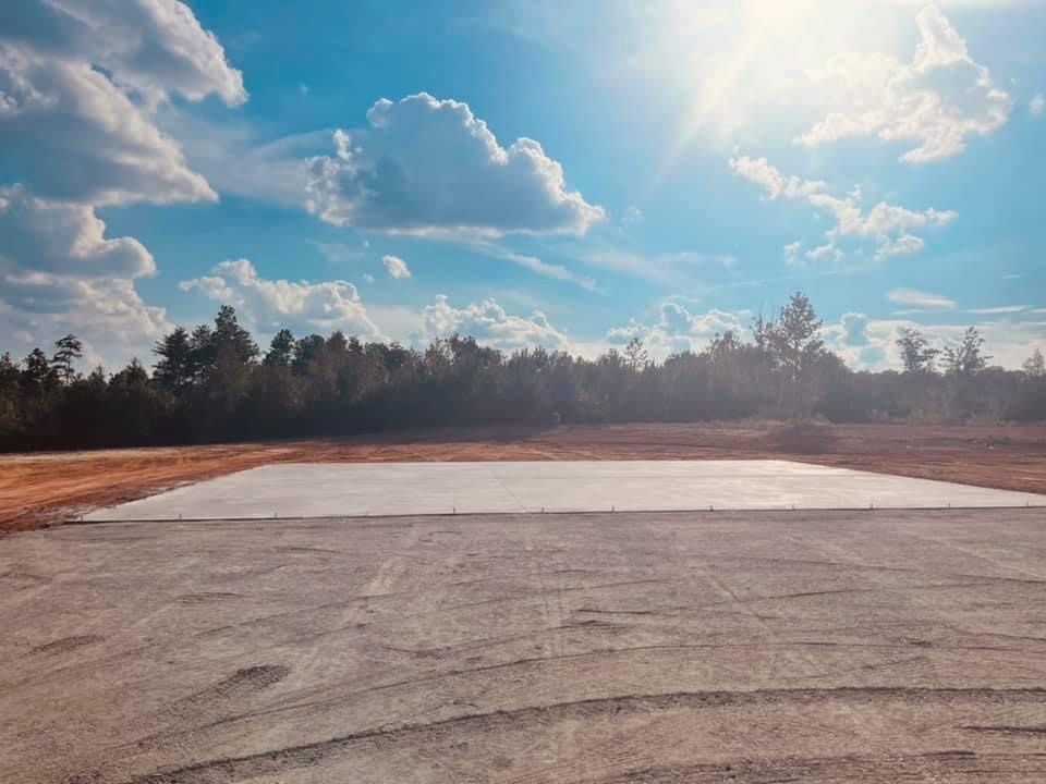 Empty concrete pad in a field beneath a bright cloudy sky and tree line