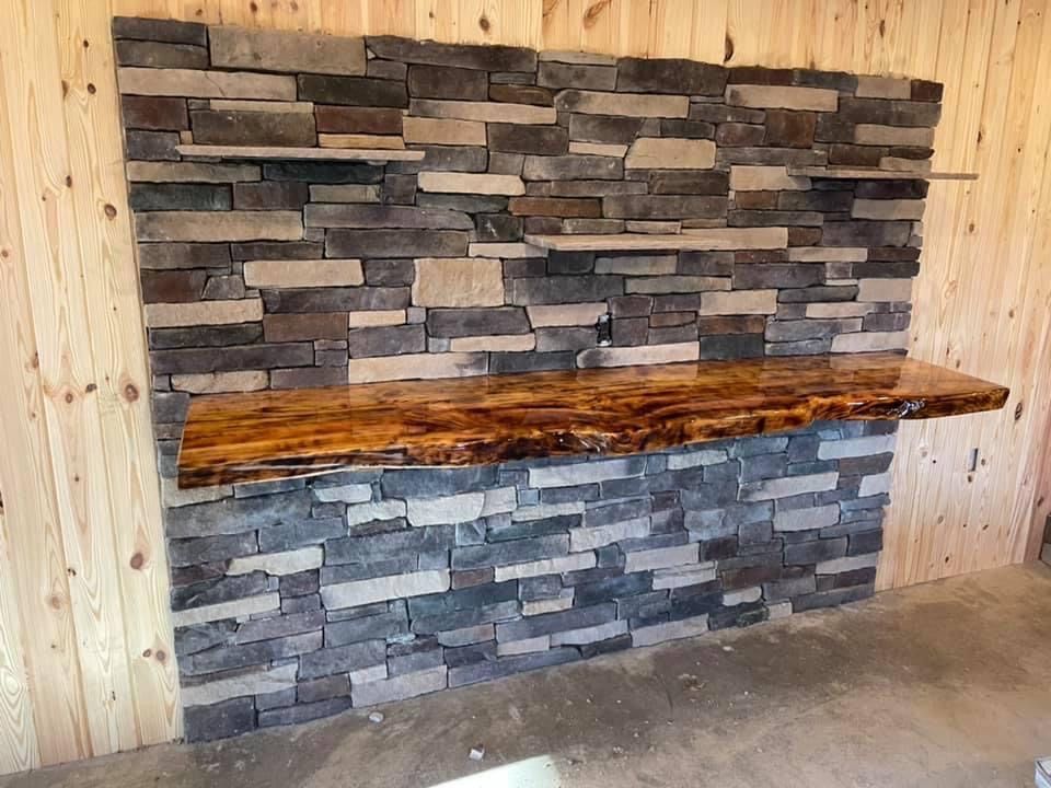 Stone veneer fireplace with a long rustic wooden mantel in a room under construction