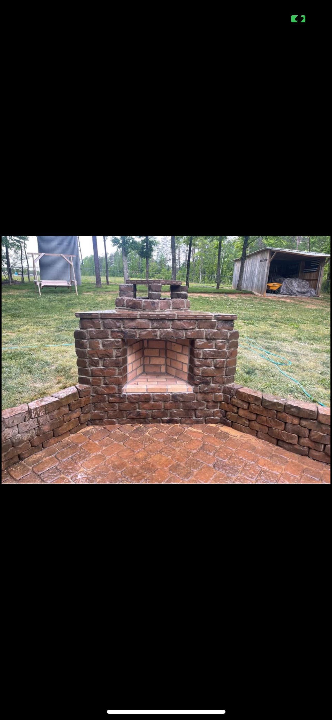 Brick outdoor oven or fireplace in a grassy yard with trees and a building in the background