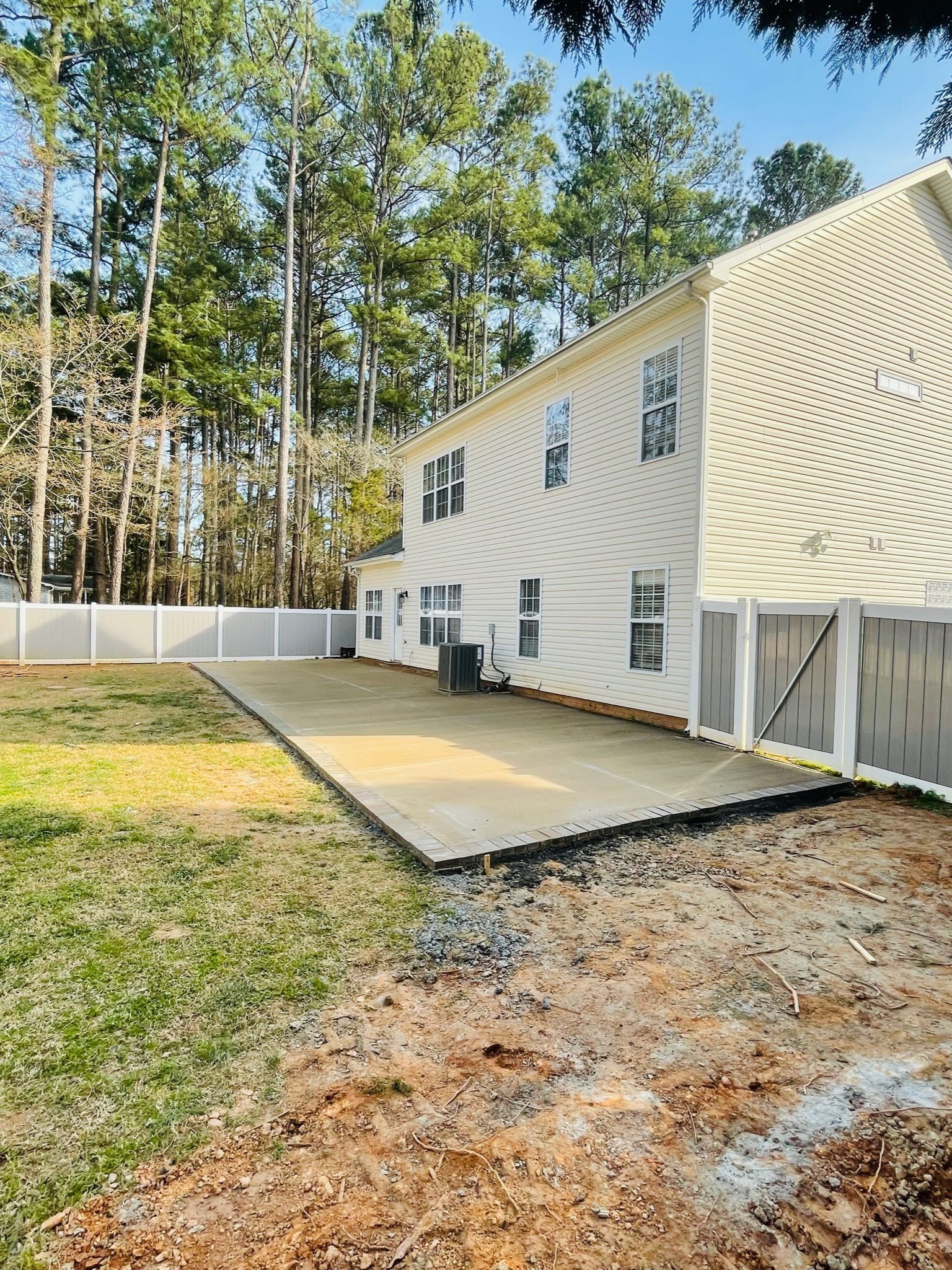 White two-story house with a patio and fenced yard beside tall trees on a sunny day
